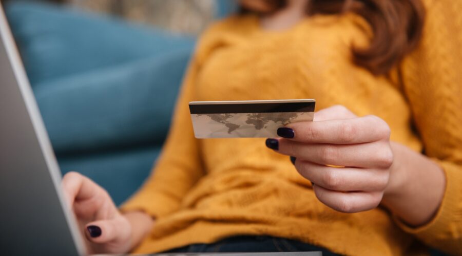Close up of a woman buying on line with bank card and laptop while sitting in the living room at home