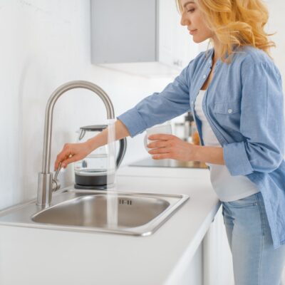 Young woman with glass at the sink on the kitchen. Female person drinks fresh water at home in the morning, healthy nutrition and lifestyle